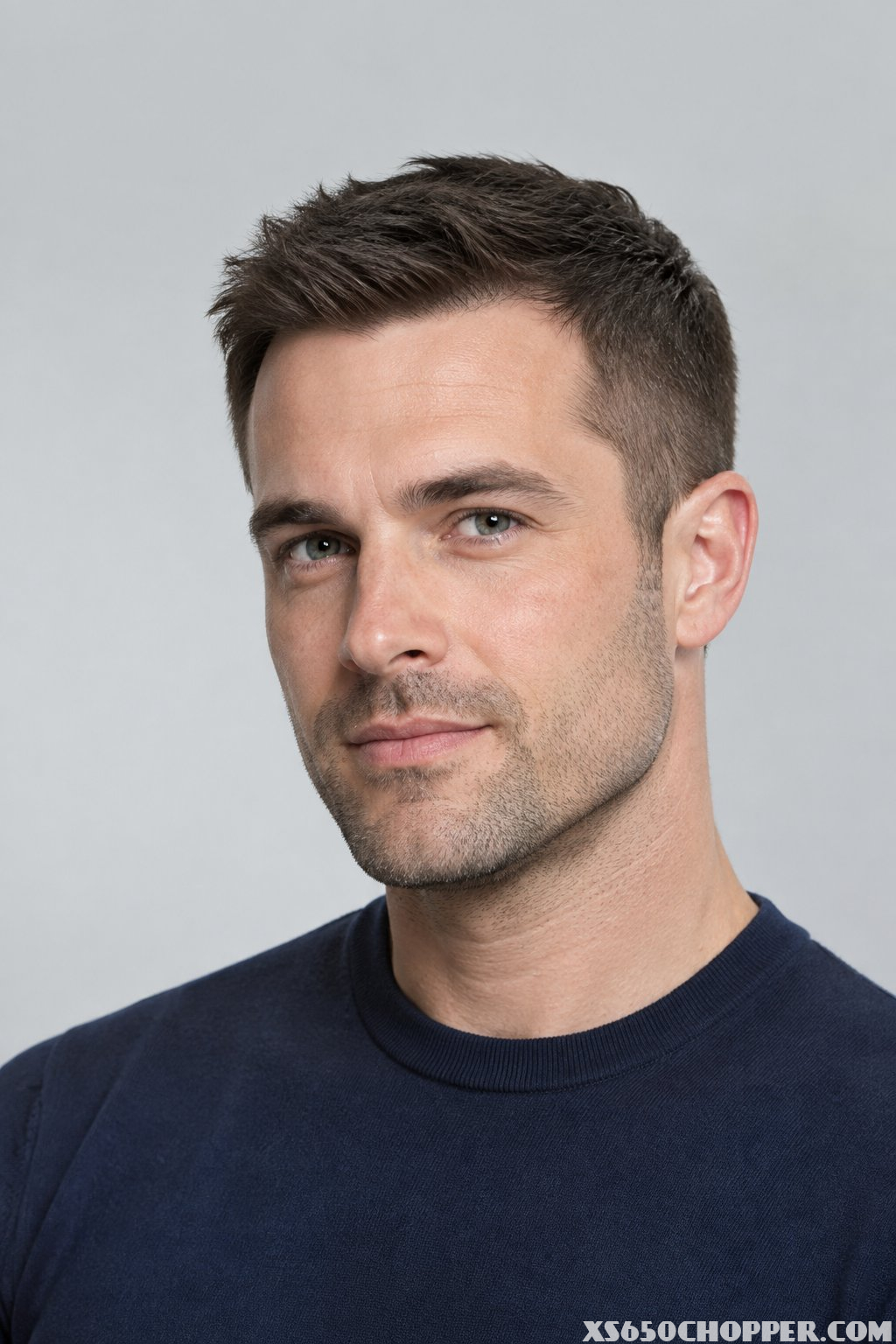 A man with a short textured crew cut and tapered sides looks toward the camera.