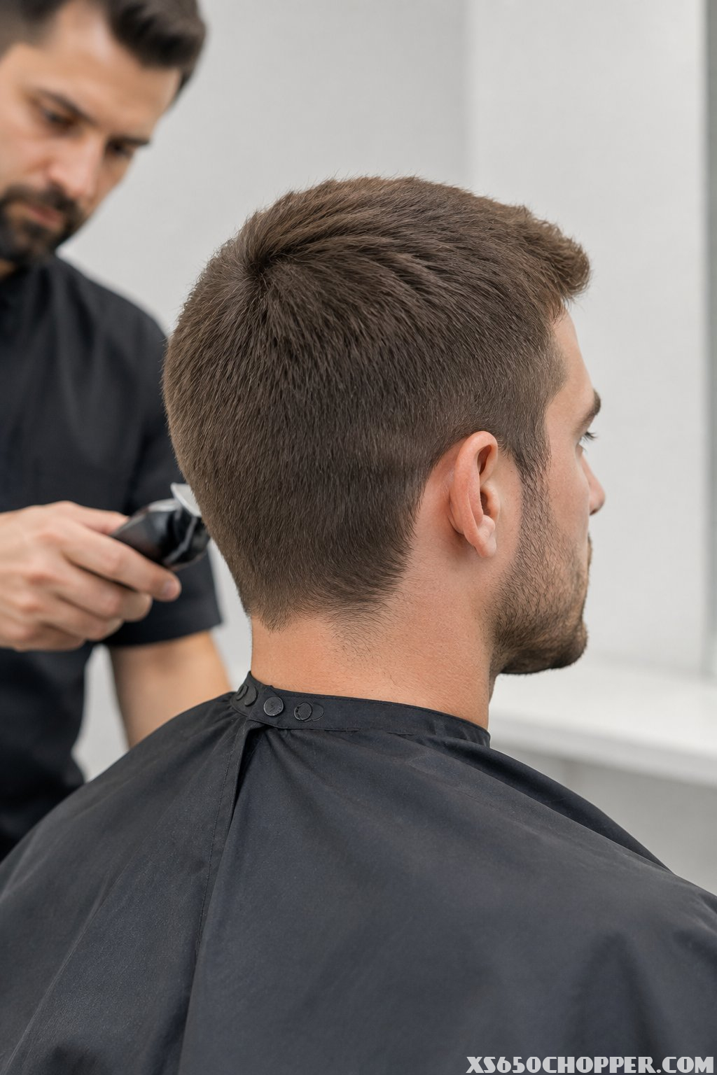 A man displaying an evenly trimmed medium-short haircut in a modern barbershop.