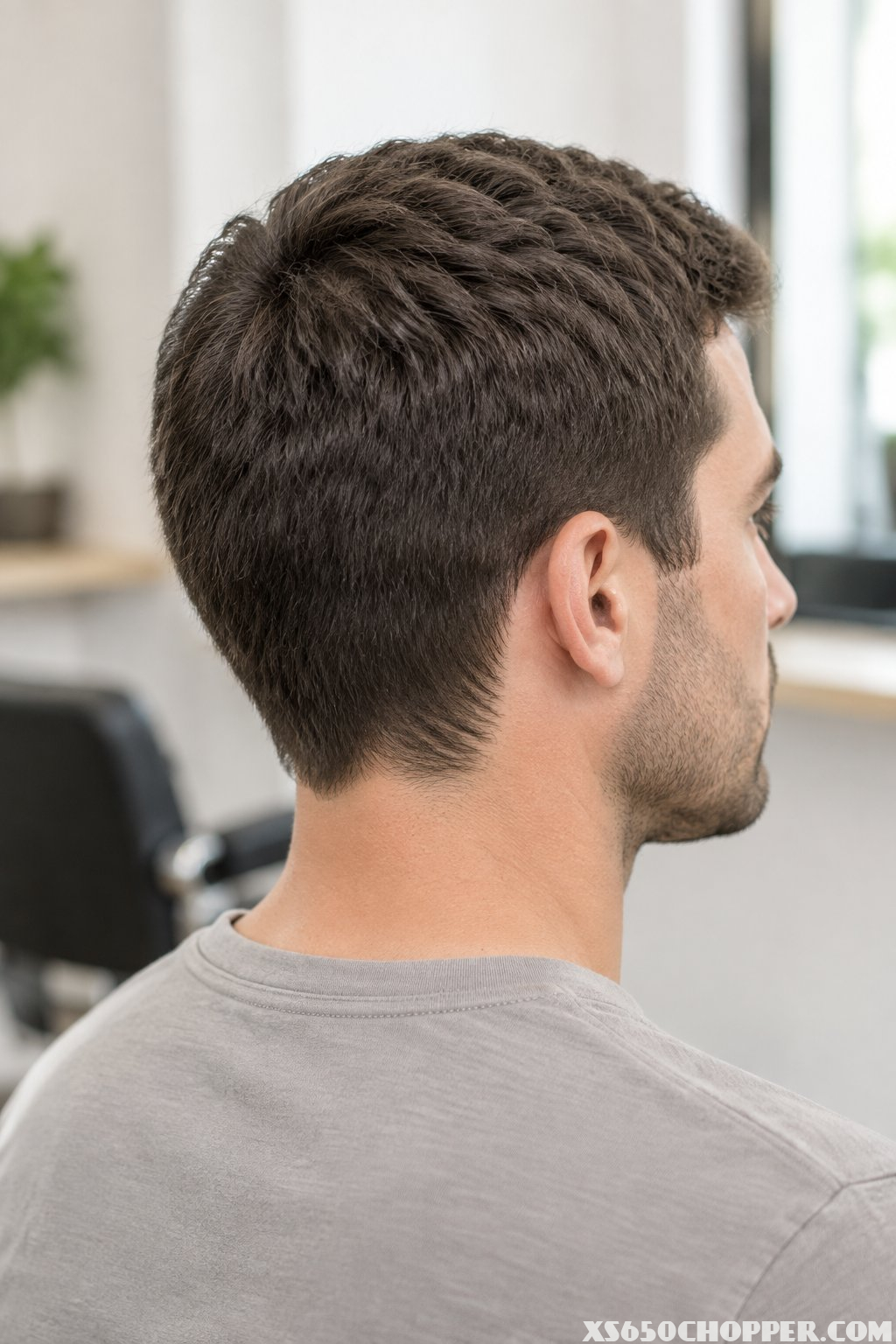 A man with evenly trimmed medium-short hair viewed from a three-quarter rear-side angle in a barbershop.