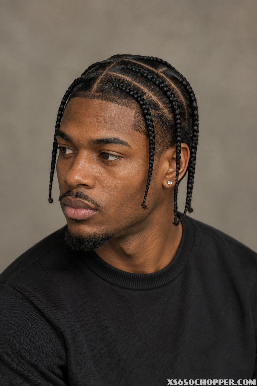 A man with neatly arranged curved braids poses against a softly blurred neutral background.
