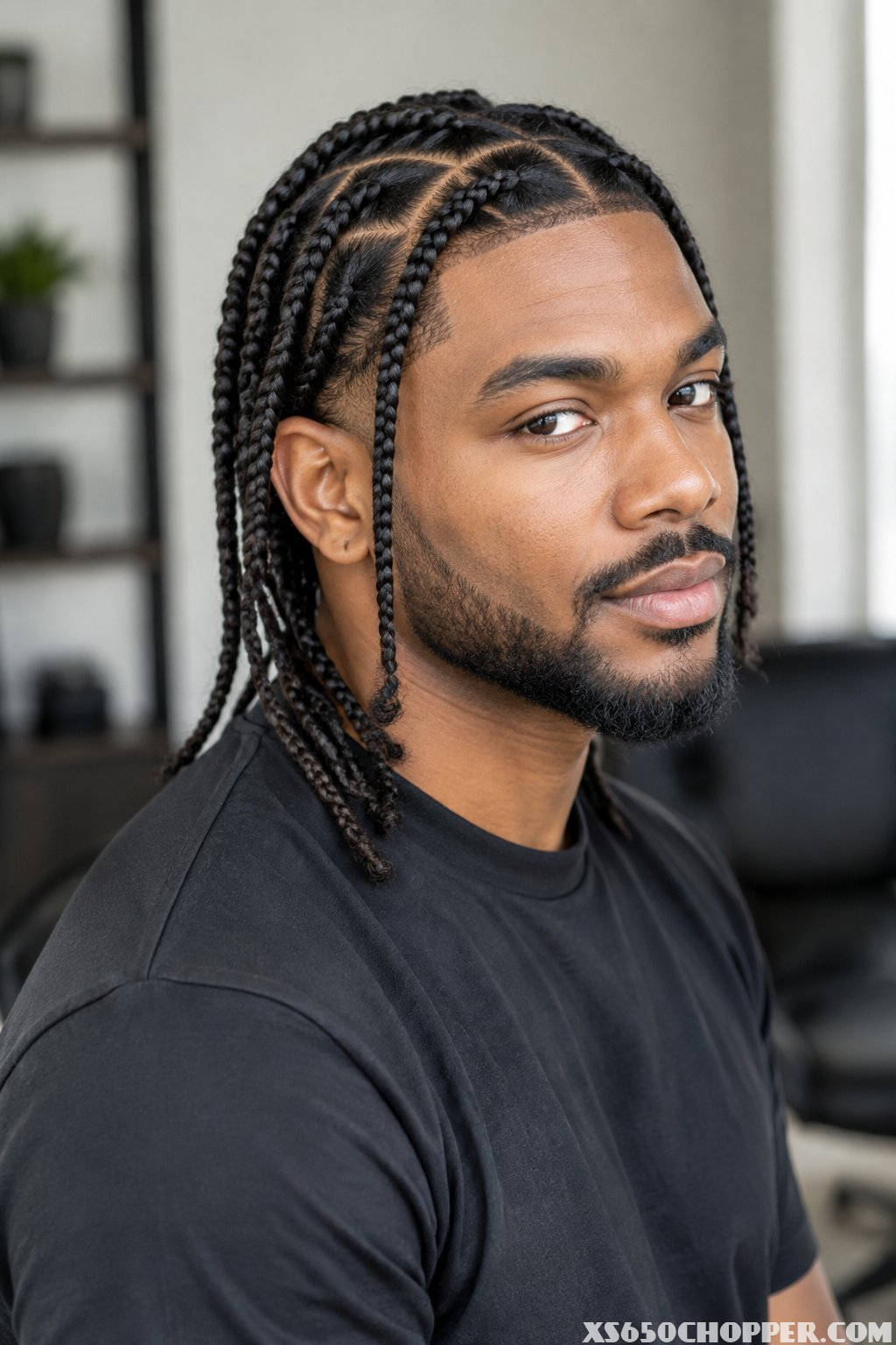A man with neatly styled individual braids poses in a modern barbershop.