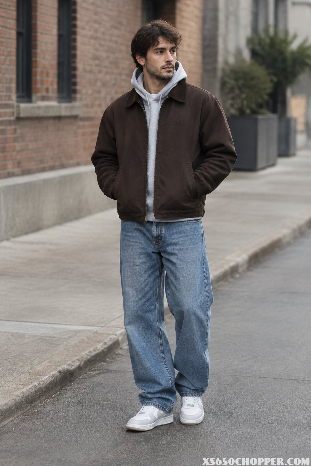 Man wearing a brown workwear jacket over a gray hoodie with loose blue jeans on an urban street.
