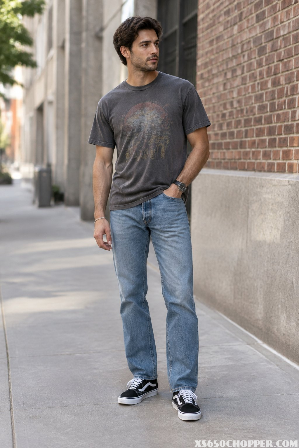 A man stands on an urban sidewalk wearing jeans, a graphic T-shirt, and black-and-white sneakers.