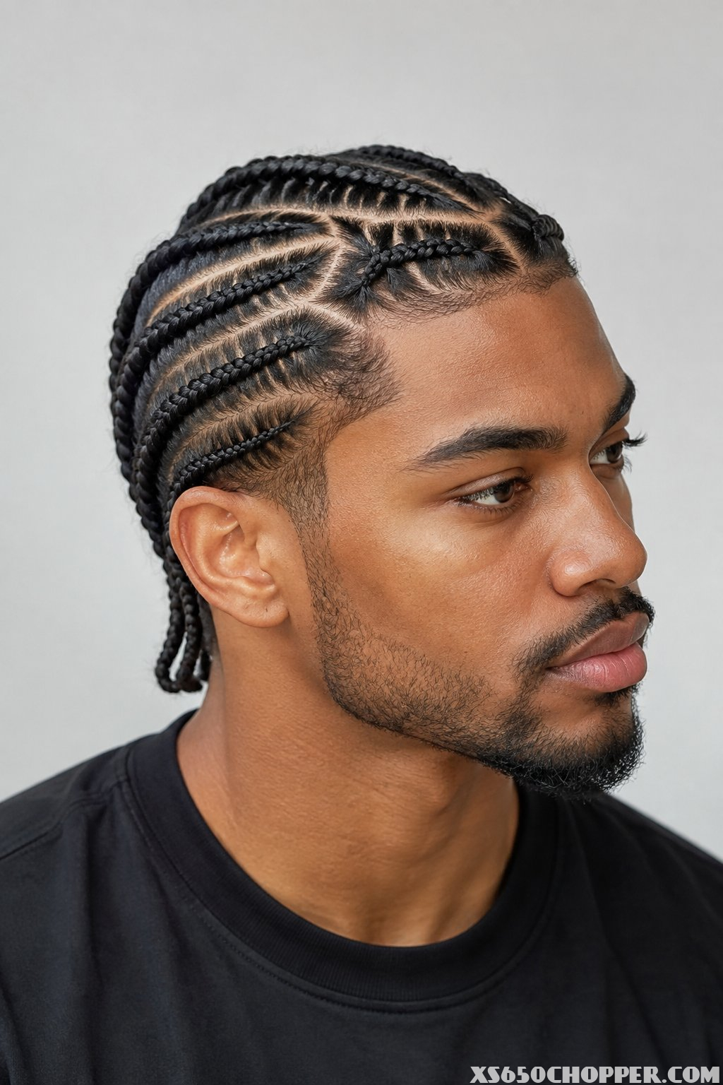 A man with neatly braided cornrows poses in a clean, modern setting.