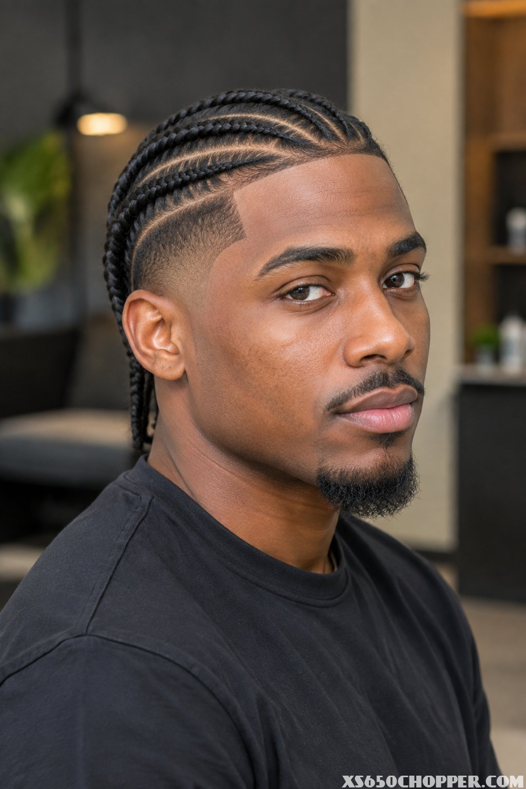 A man with neat feed-in cornrows and a burst fade poses in a barbershop.