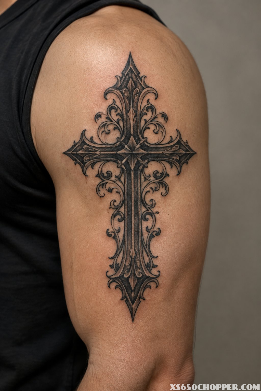 A close-up of a Gothic cross tattoo with ornate filigree on a man's forearm.