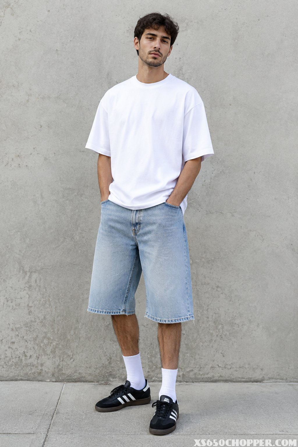 A man wearing a white T-shirt, light denim knee-length shorts, white socks, and black-and-white sneakers.