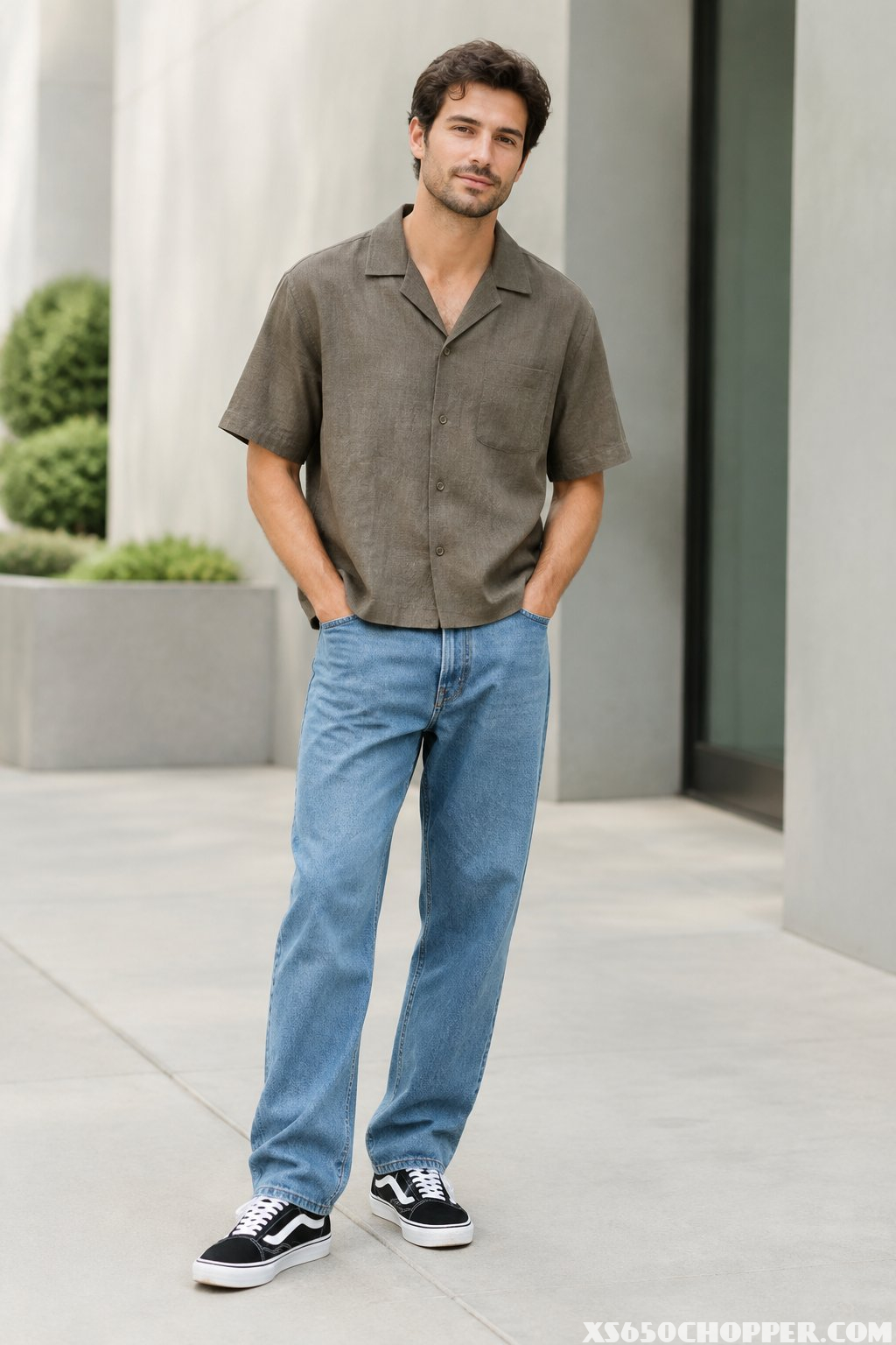A man wearing a cropped casual shirt, relaxed jeans, and black-and-white sneakers stands in an urban setting.