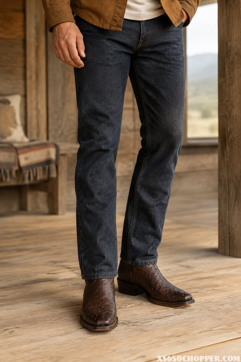 A man wearing cowboy boots and jeans stands indoors.