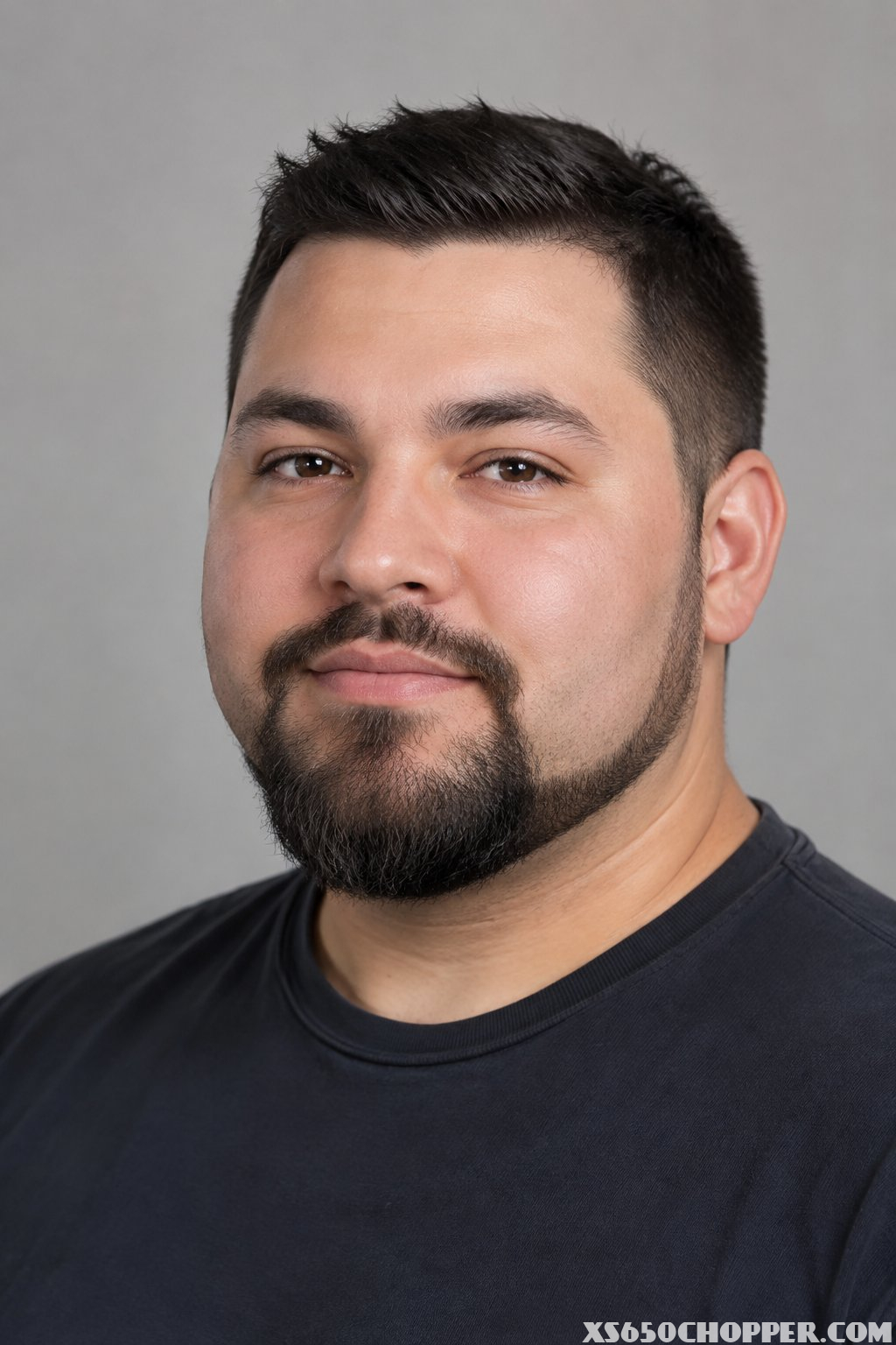 A man with a round face and a neatly shaped full goatee.