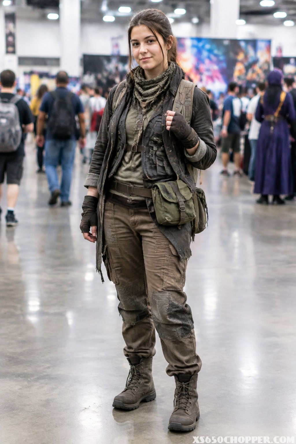 A cosplayer in layered scavenger clothing stands in a convention hall.