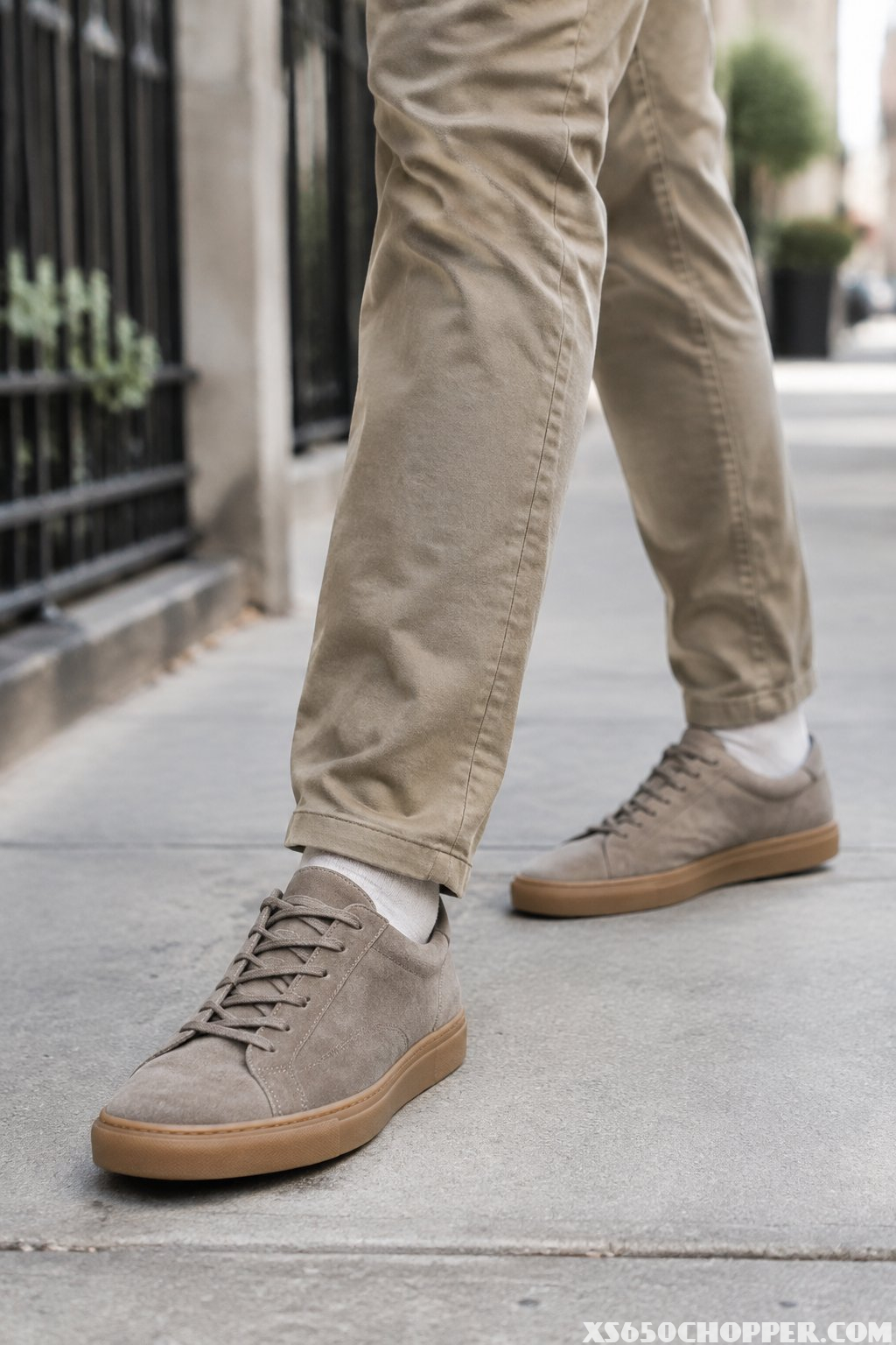 A man walks along a sidewalk wearing suede sneakers with gum soles.