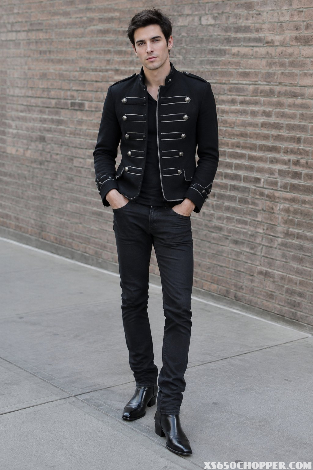 A man wearing a black military-style jacket, black jeans, and pointed-toe boots.