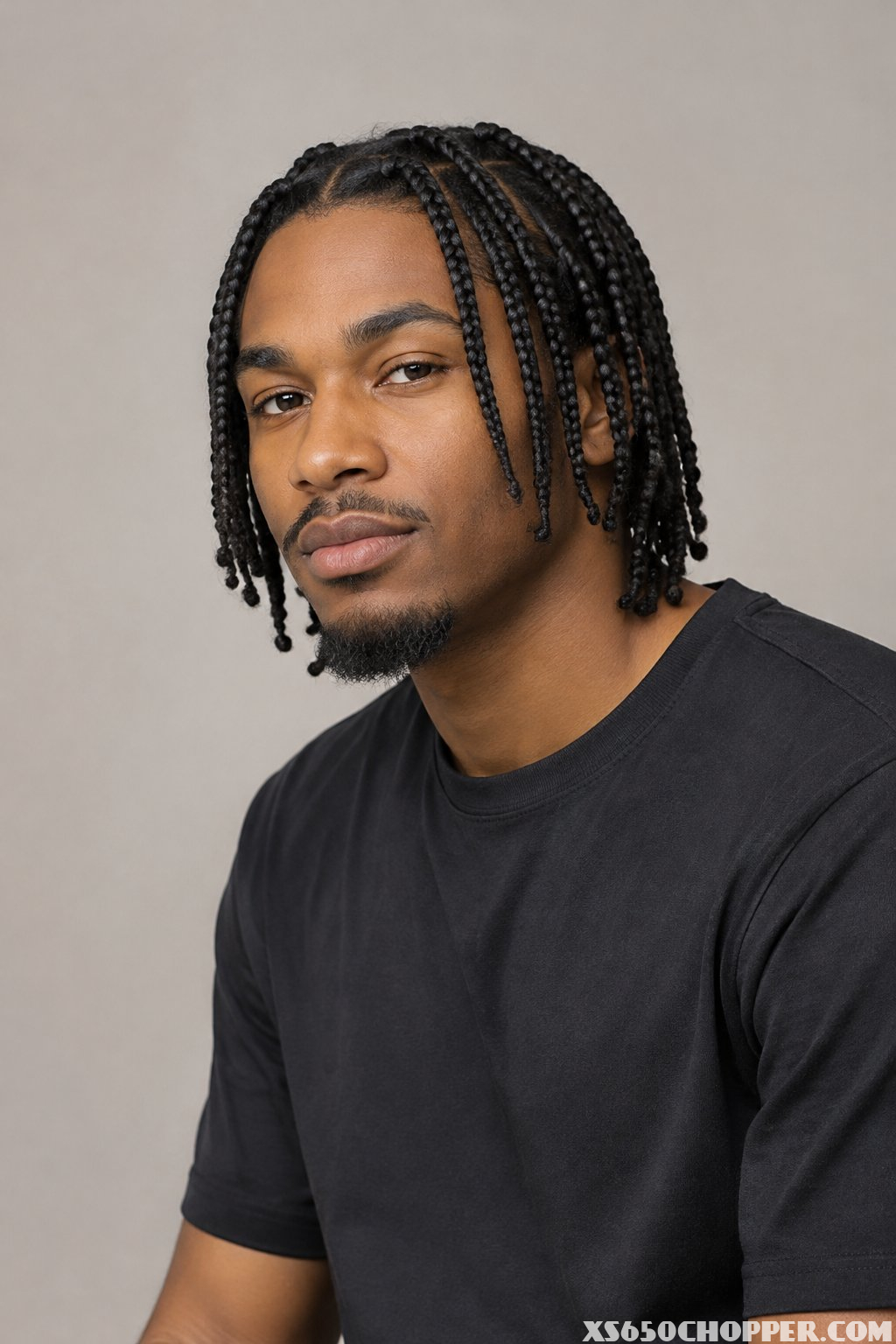 A man with braided hair poses against a plain background.
