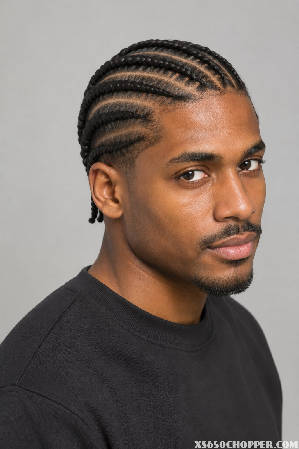 A man with short diagonal cornrows looks toward the camera.