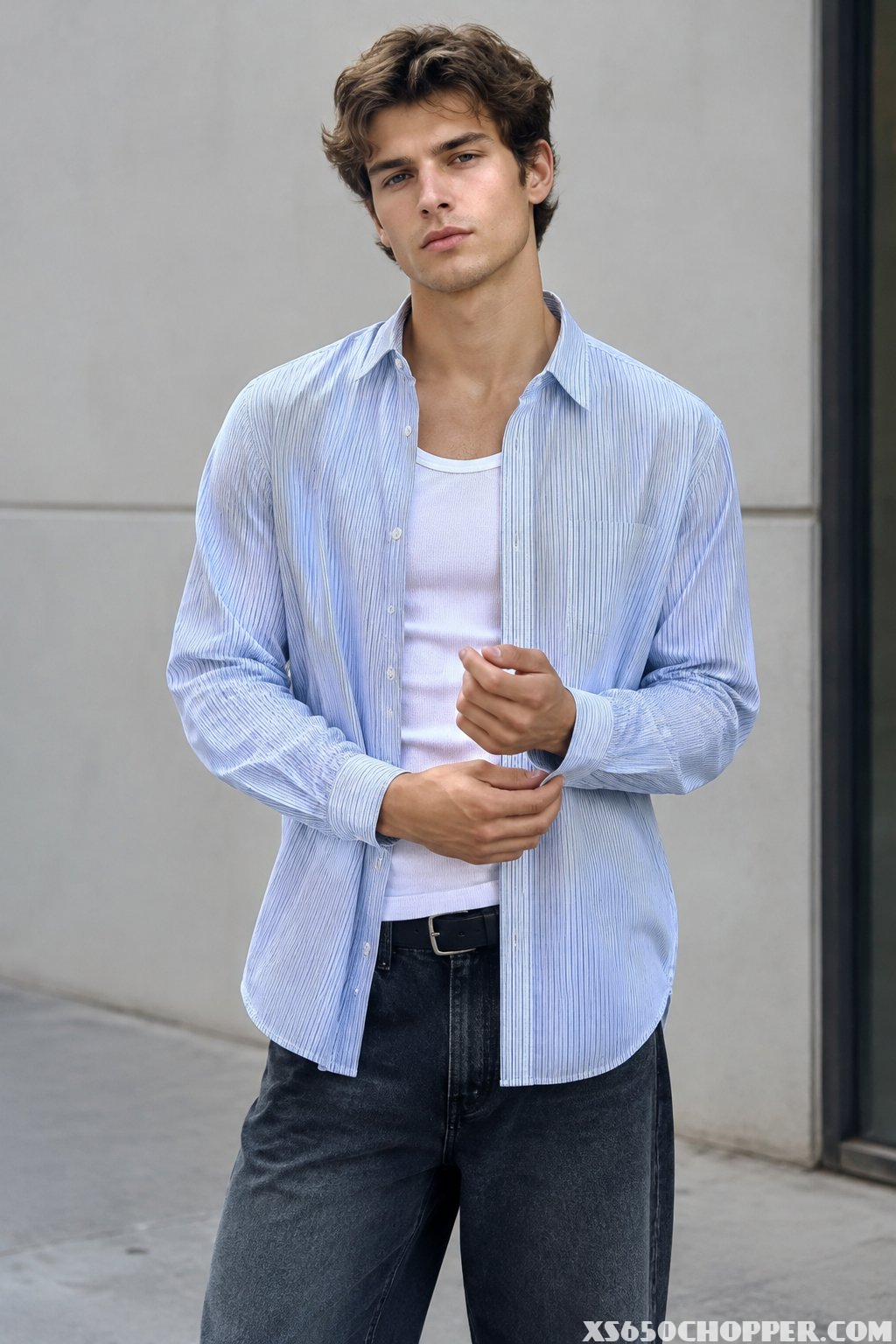 A man wearing an open pinstripe shirt over a white tank top.