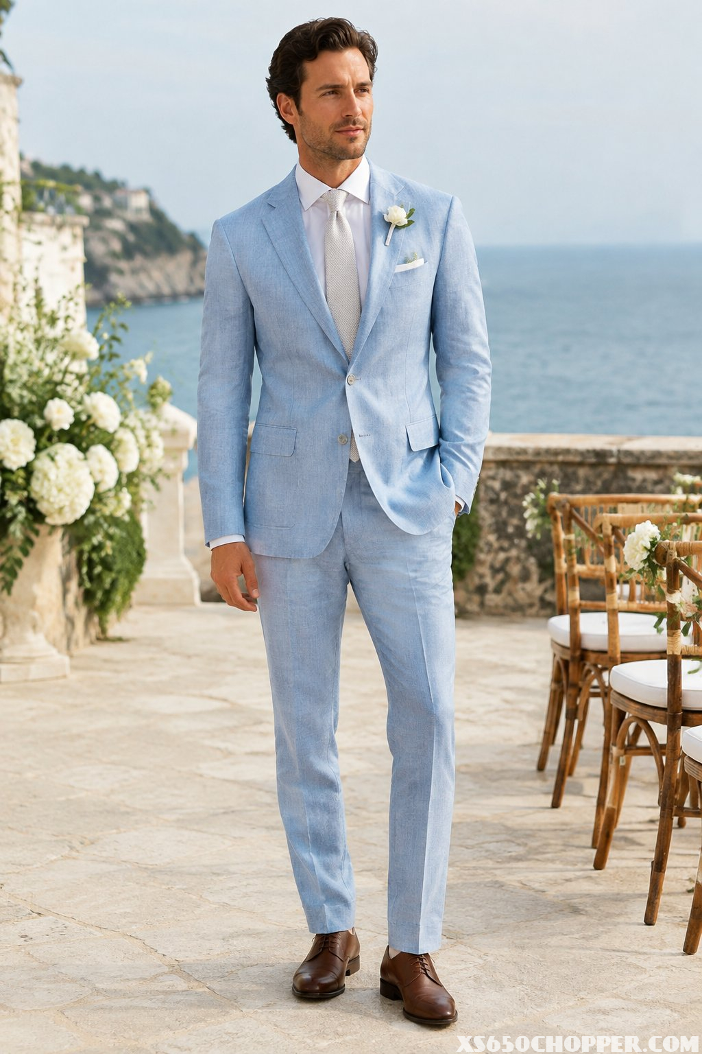 A man in a pale blue suit stands at a seaside wedding venue.