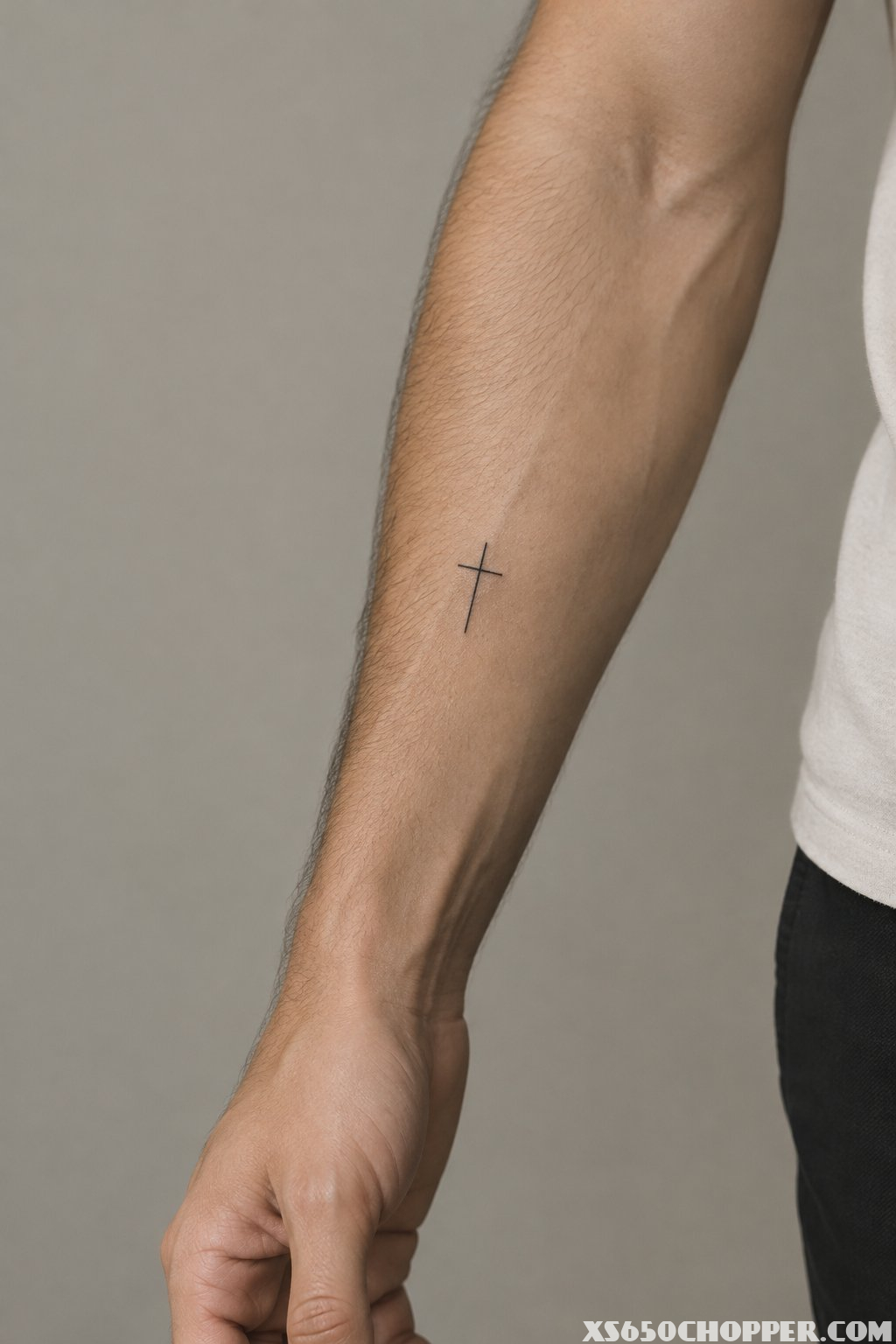 A man’s forearm with a small cross tattoo.