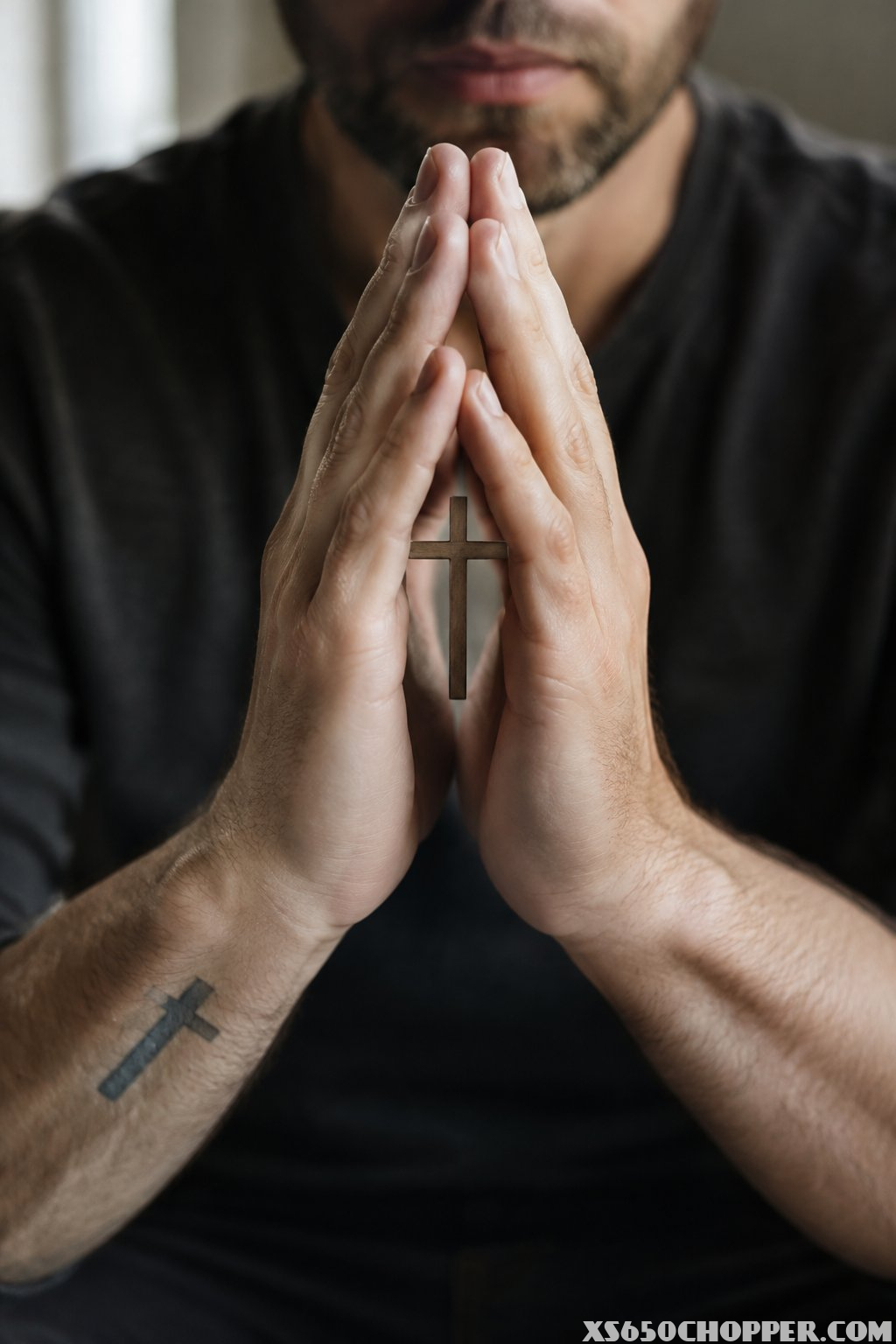 A man holds his hands together in prayer, framing a cross.
