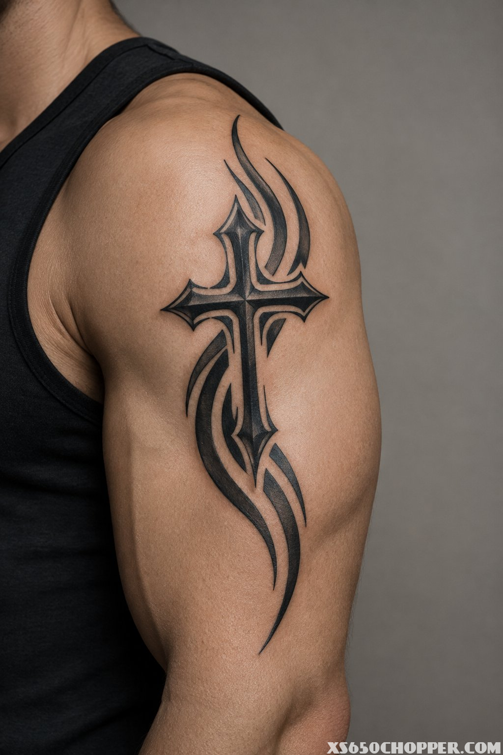 A man’s upper arm with a black tribal cross tattoo and sweeping curved lines.