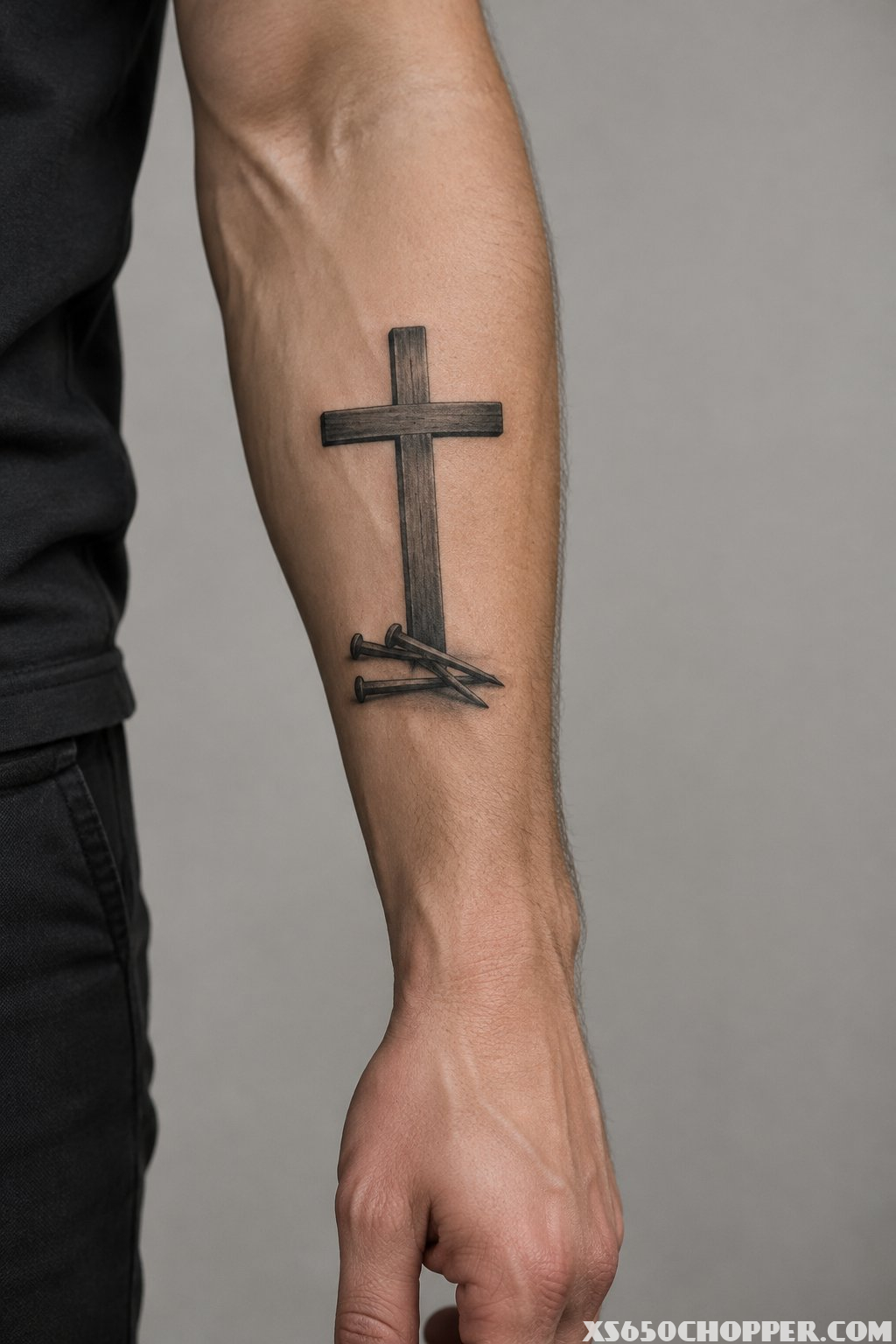 A man’s forearm with a cross tattoo and three nails at its base.