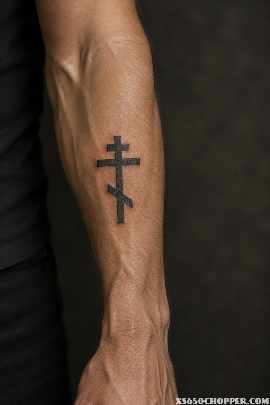 A man’s forearm displaying a black Orthodox cross tattoo with three crossbars.