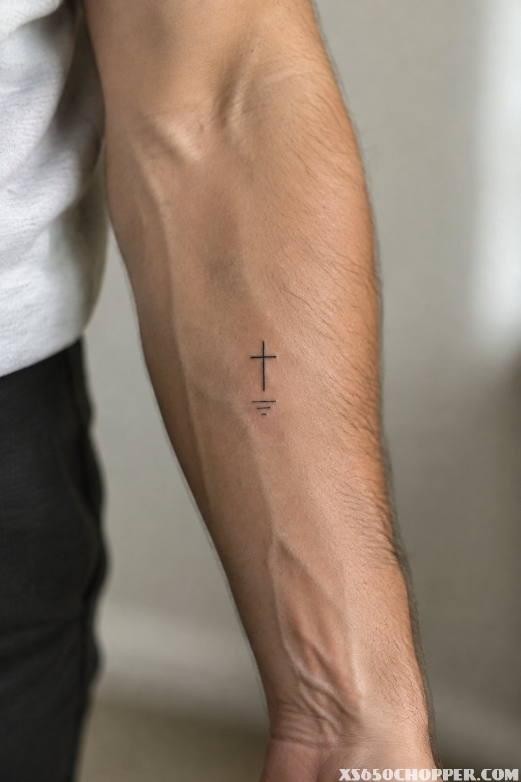 A man’s forearm with a small cross tattoo.