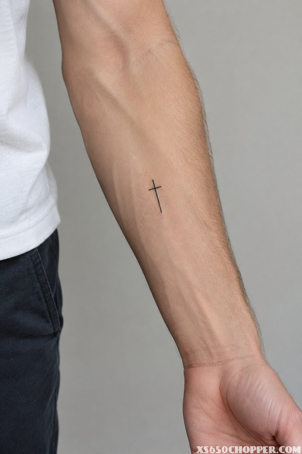 A man’s inner forearm with a small cross tattoo.
