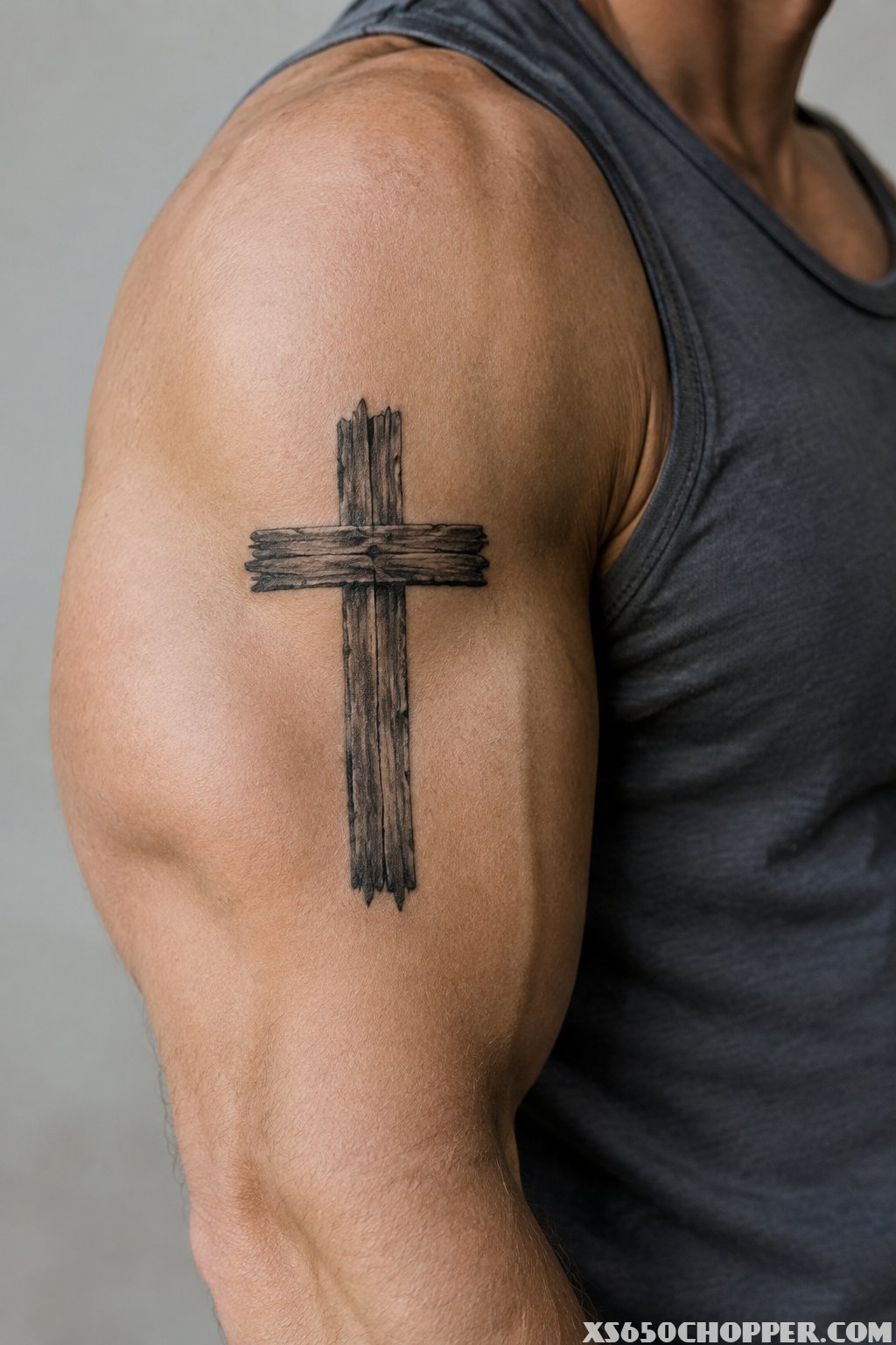 A man’s upper arm with a weathered wooden cross tattoo on the bicep.